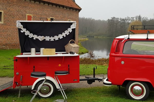 Roter Sektbar-Anhänger mit geöffneter Bar neben dem VW T2-Bus